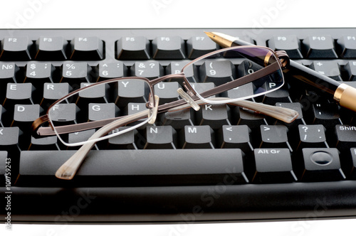 pen with a golden feather and glasses is on the black keyboard