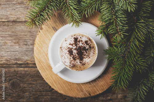 A cup of coffee with the branches of the Christmas tree on a woo