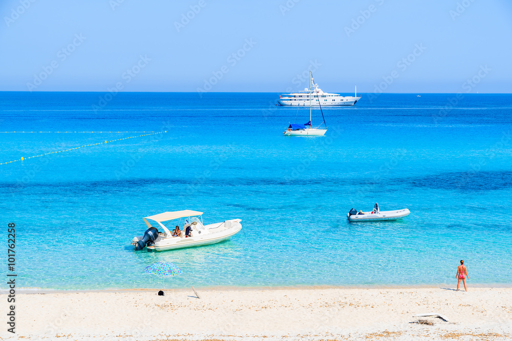 Fototapeta premium Boats on azure sea and young woman standing on Saleccia beach , Corsica island, France