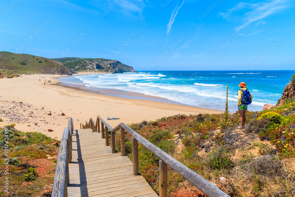 Walkway to Praia do Amado beach and young woman tourist looking at sea, Algarve region, Portugal