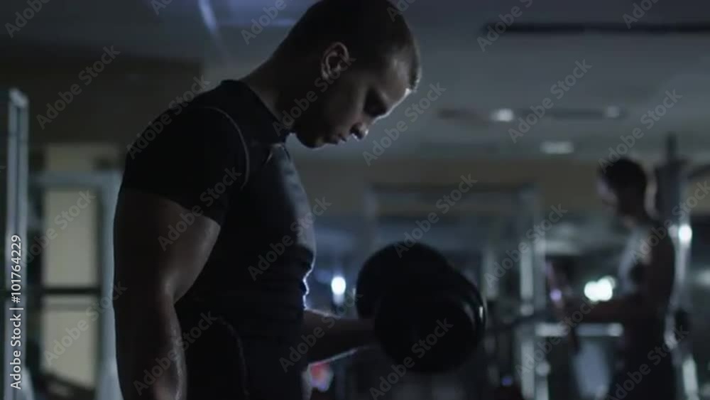 Handsome fit sporty man does dumbbell curl exercises in dark gym. Shot on RED Cinema Camera. Handsome fit sporty man does dumbbell curl exercises in dark gym. Shot on RED Cinema Camera.