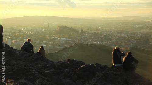 Tourists take in a view of distant Edinburgh, Scotland from the top of the King's Seat hike at sunset.