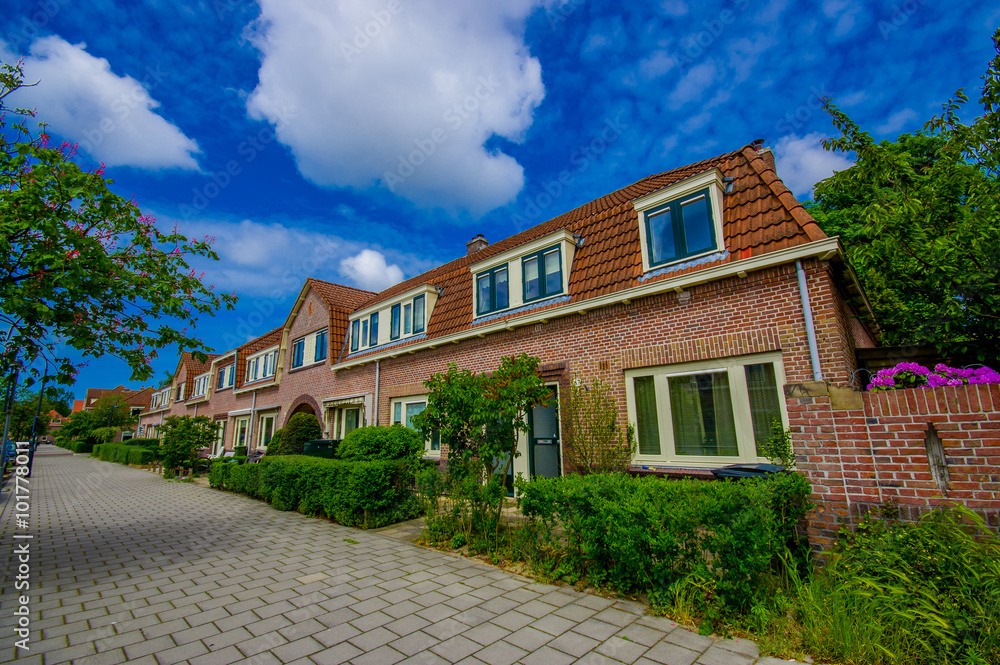 Harlem, Amsterdam, Netherlands - July 14, 2015: Very charming and traditional Dutch neighbourhood, red bricks nice townhouses stretching down street, beautiful blue skies, green trees around