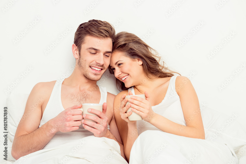 Cute young couple sitting together with cups and smiling Cute young couple sitting together with cups and smiling