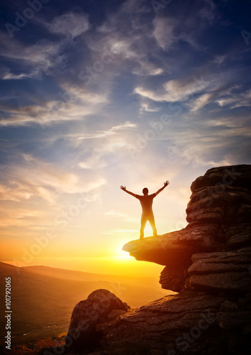 A person reaching up from a high point, set against a sunset. Expressing freedom photo
