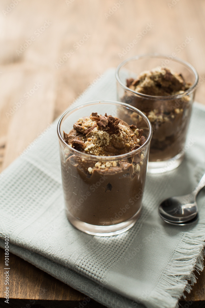 Vegan chocolate mousse (pudding) in a glass bowl with a silver spoon. Rustic tablecloth in the background, close up. Vegan chocolate mousse (pudding) in a glass bowl with a silver spoon. Rustic tablecloth in the background, close up.