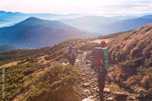 Two Hikers walking on Mountain Path Sunset Mountains Background