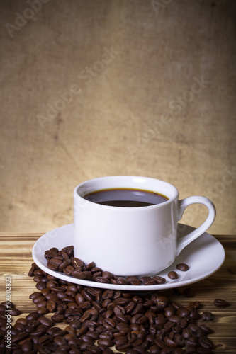Coffee beans and coffee in white cup on wooden table opposite a