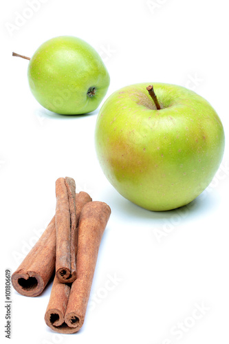 Two ripe green apples and three pieces of cinnamon over white.