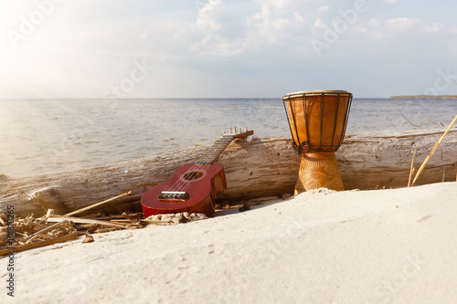 Ukulele and ethnic drum on a sunny beach over sky background.
