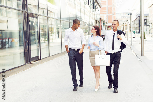 Business people walking trough passage, looking each other and smiling.