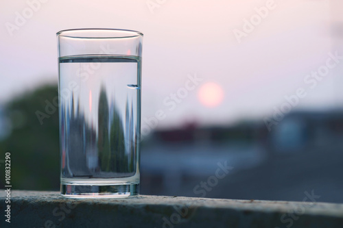 Glass with water / Glass with water on the balcony with sunset blur background.
