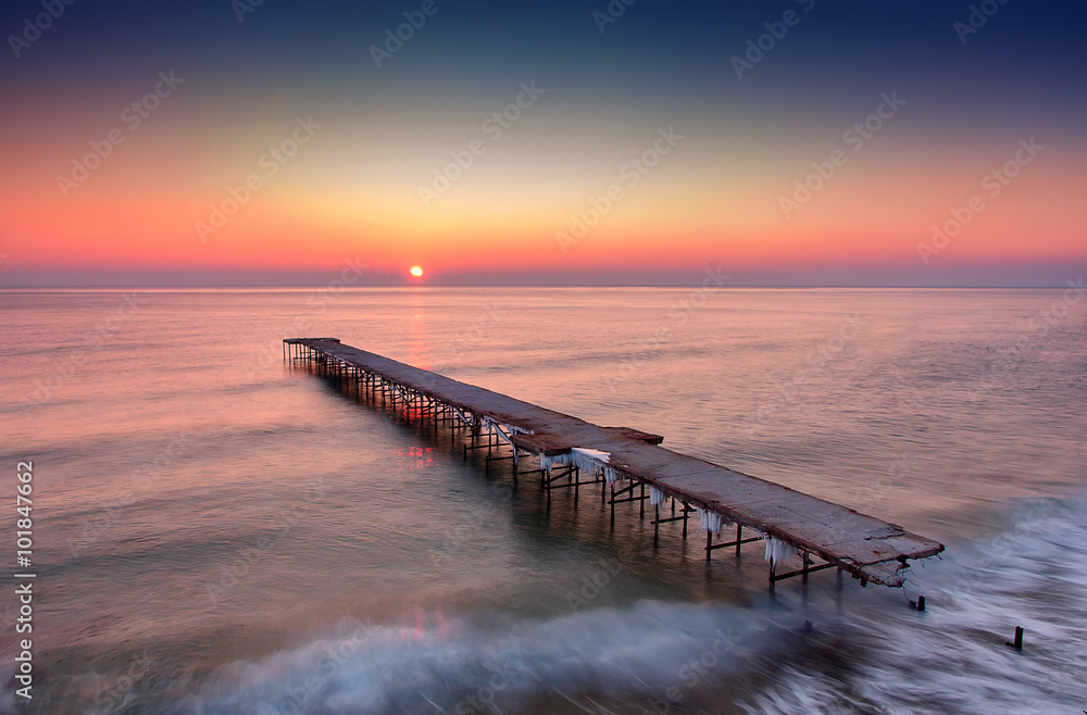 Obraz premium winter sunrise long exposure landscape with old broken bridge in the sea