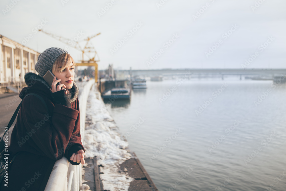 Young woman standing by the river and talking on the phone
