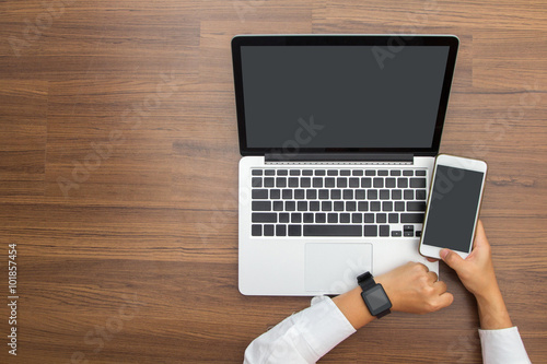 Female hand with smartwatch with holding mobile phone on laptop