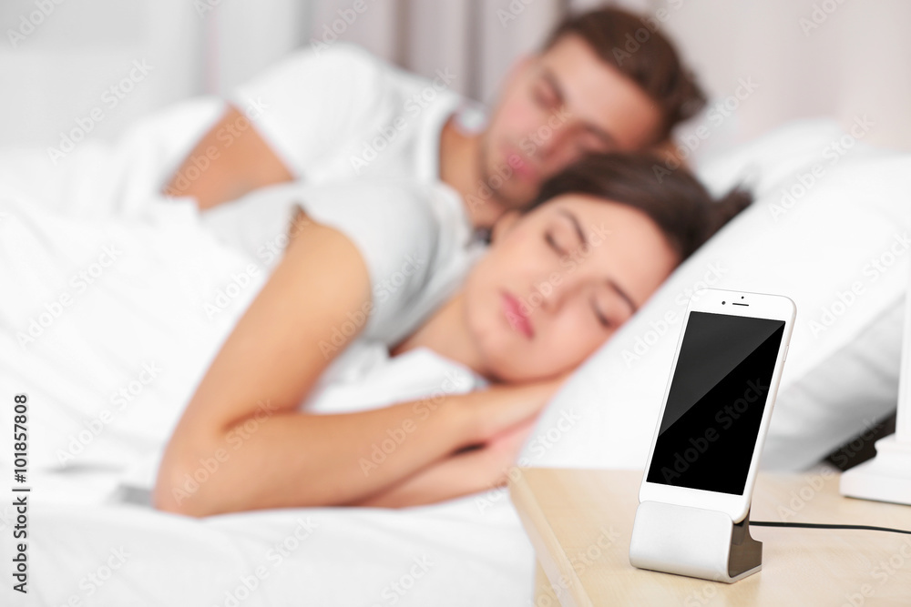 Happy couple waking up with mobile alarm clock Happy couple waking up with mobile alarm clock