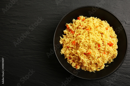 Stewed rice with a carrot on a plate over black background