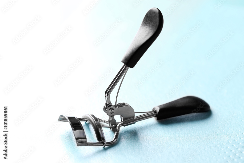 Eyelash curler with black handles on a blue background, close up Eyelash curler with black handles on a blue background, close up
