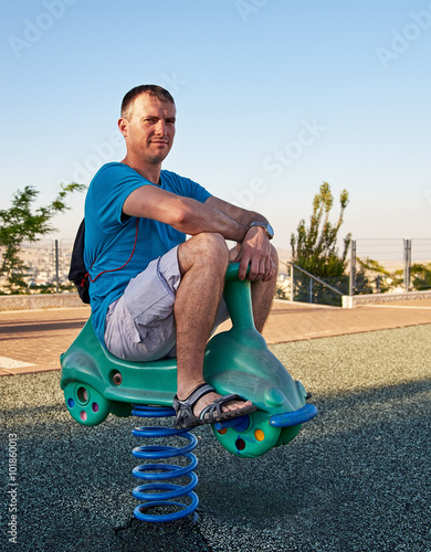 Obraz na płótnie Adult handsome man reliving childhood playing in a children playground riding on spring seat
