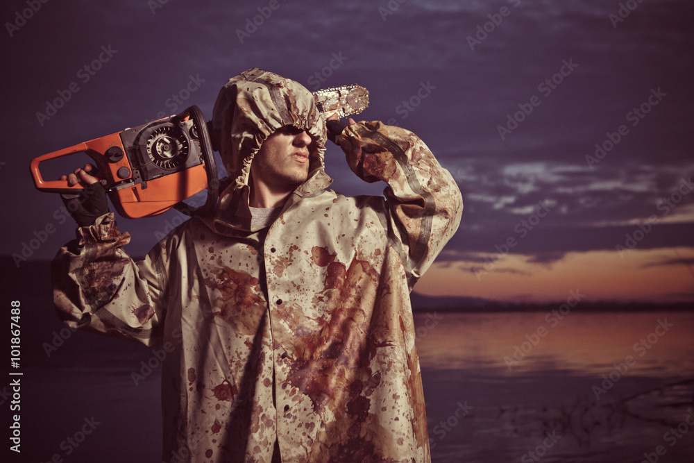 Fototapeta premium Maniac with the chainsaw on the sunset background.