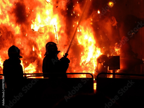 Great Fire of burning figures during the Las Fallas (festival in Spain, Valencia) on the background of two silhouettes of fire fighters  photo