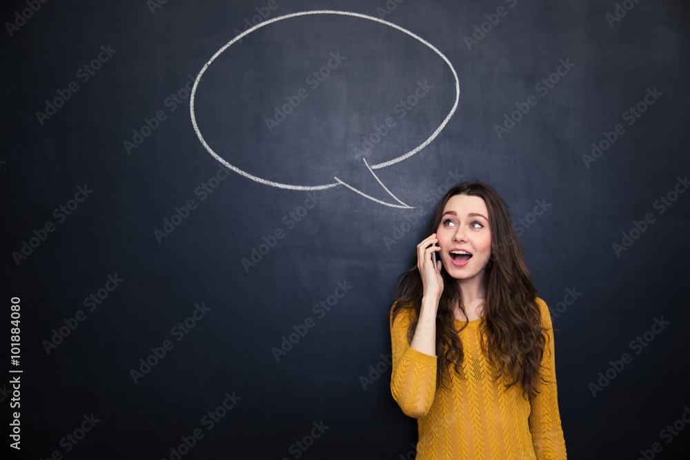 Cheerful woman talking on cellphone over blackboard with  speech bubble