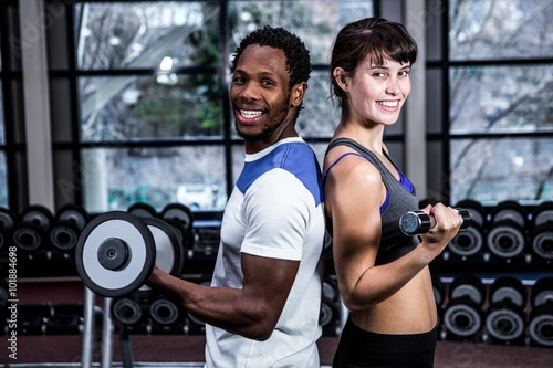 Fit couple lifting dumbbells back to back 