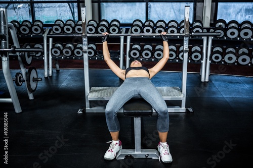 Fit woman lifting barbell while lying on bench 