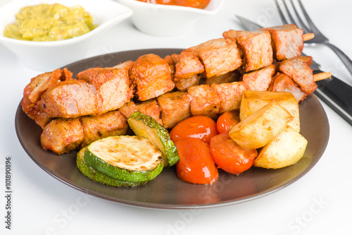 skewered meat and vegetables on plate on white background