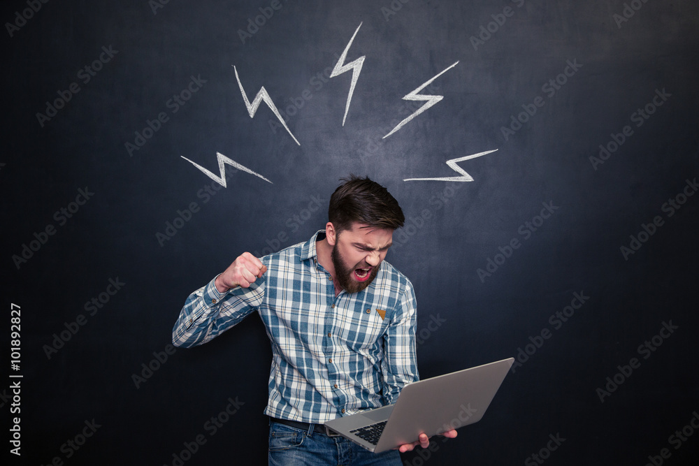 Fotografie Aggressive man going to break laptop over chalkboard background