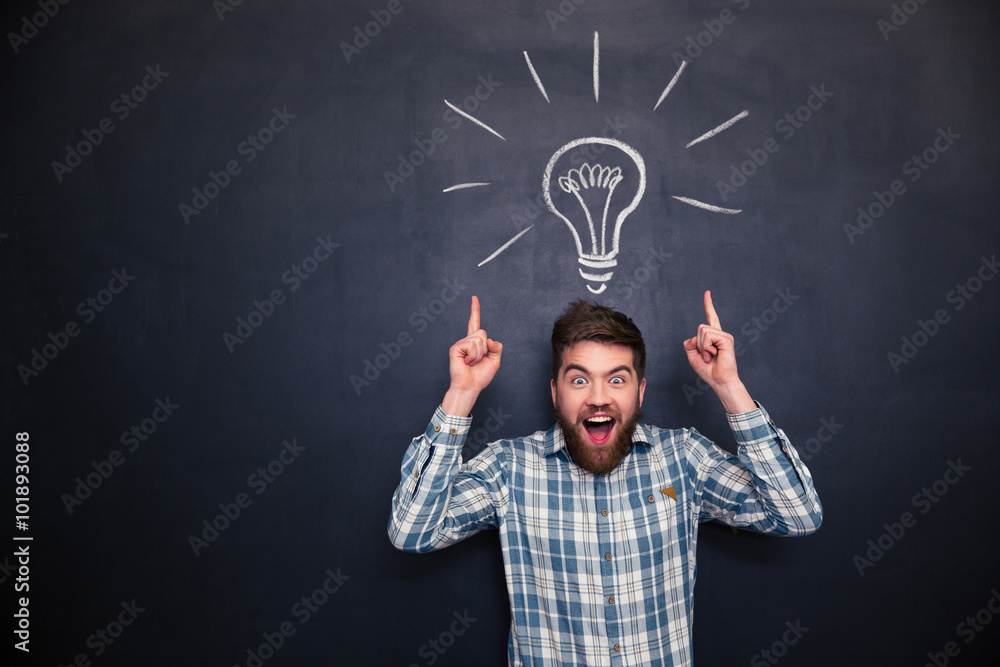 Fotografie Surprised man pointing up with both hands over chalkboard background