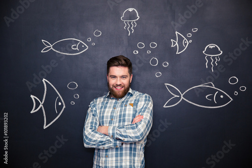 Cheerful man standing over blackboard with drawn fishes and jellyfishes