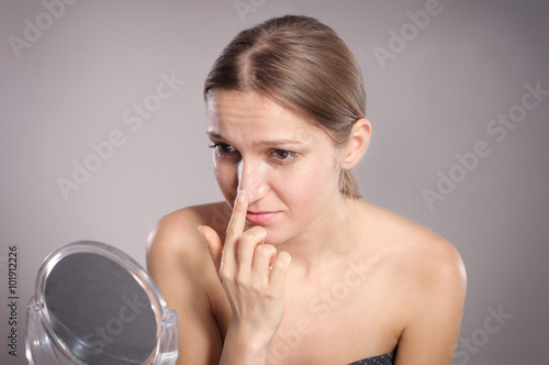 Young woman checks her nose in the mirror