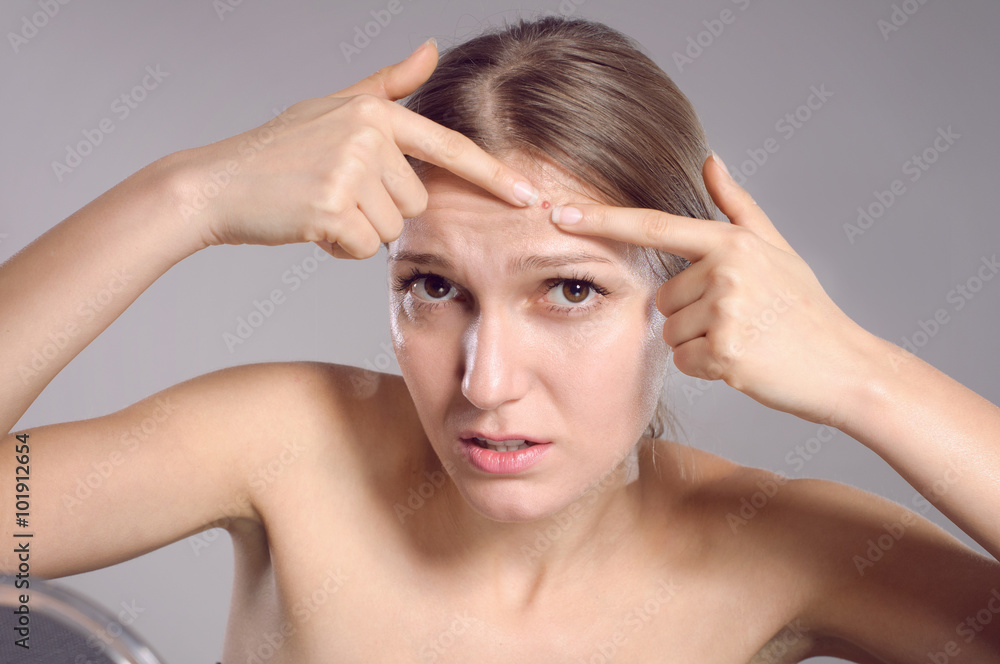 Fototapeta premium Young woman squeeze her acne in front of the mirror