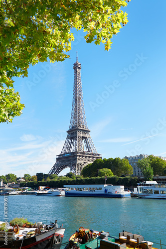 Eiffel tower and Seine river view with green tree branches in a sunny summer day