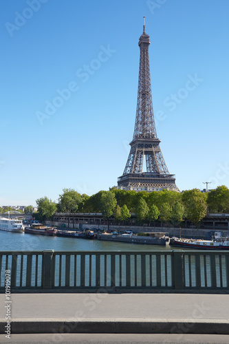 Eiffel tower and empty sidewalk bridge on Seine river in a clear sunny day