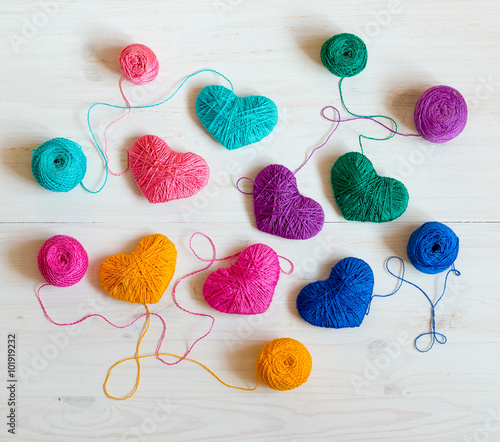 Multicolored Hearts with a balls of thread on white wooden backg