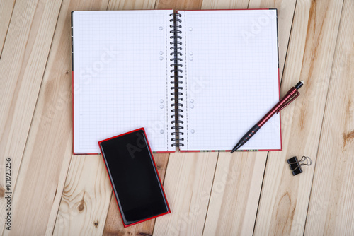 Red Smart Phone With Blank Black Screen, Notepad And Pencil On Wooden Desk.