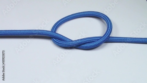 Simple overhand knot made from blue synthetic rope, tightening on white background