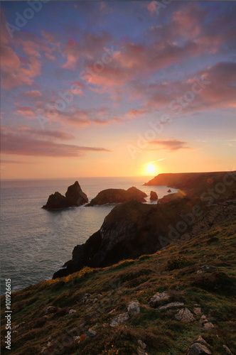A rugged coastal sunset from a cliff top. The sun setting behind the ocean's horizon in Cornwall.