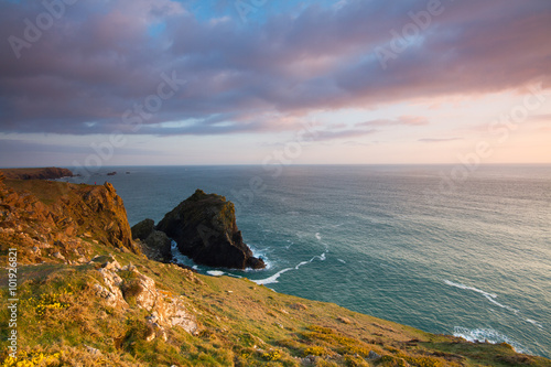A rugged coastal sunset from a cliff top. A sunlit seascape of the ocean in Cornwall.