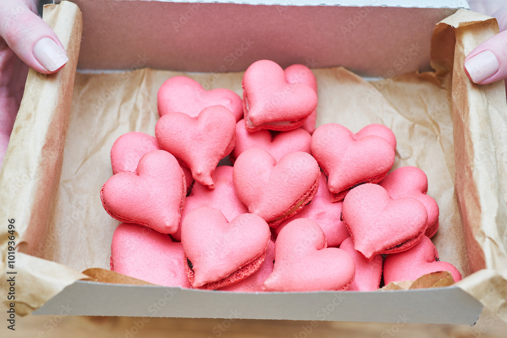 The box of heart-shaped macarons with flowers and ribbon on a wooden table. Creative gift for Valentine's Day The box of heart-shaped macarons with flowers and ribbon on a wooden table. Creative gift for Valentine's Day