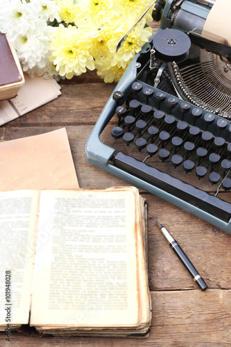 Vintage black typewriter with old books and flowers on wooden table, outdoors