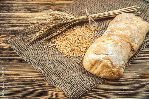 a ciabatta bread with wheat on stackcloth on a wooden rustic background photo