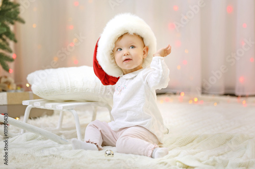 Funny baby girl wearing red hat in Christmas living room