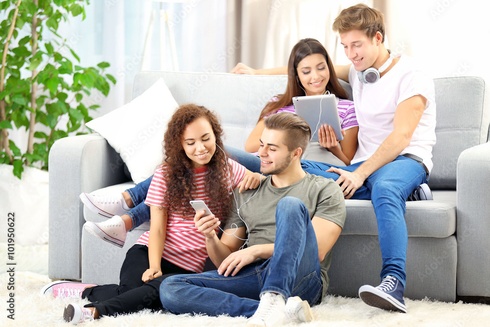 Two teenager couples listening to music with different devices in living room