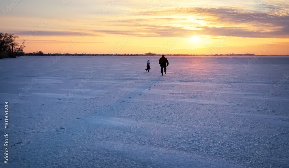 Dad is running for her daughter on a frozen river at sunset. 
