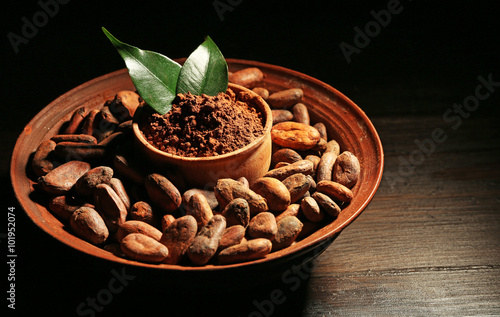 Bowl with aromatic cocoa harvest on wooden background, close up