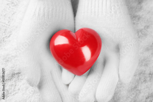 Hands in warm white gloves holding red heart on snowy background