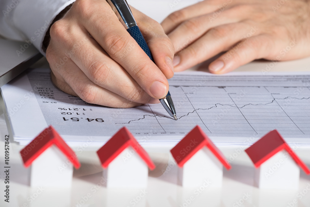 Businessman Preparing Financial Chart With House Models At Desk Businessman Preparing Financial Chart With House Models At Desk